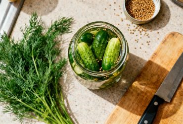 Bocal en verre rempli de cornichons maison avec aneth et graines de moutarde sur un plan de travail de cuisine