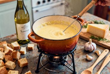 Fondue savoyarde au fromage fondu dans un caquelon traditionnel, entourée de morceaux de pain et de gousses d'ail