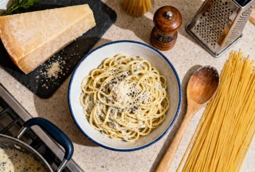 Bol de pâtes cacio e pepe crémeuses avec sauce au pecorino romano et poivre noir, accompagné de fromage et moulin à poivre