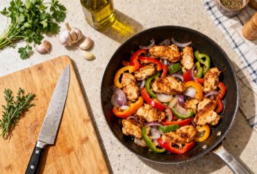 Sauté de dinde doré avec poivrons multicolores et oignons dans une poêle, sur un plan de travail de cuisine