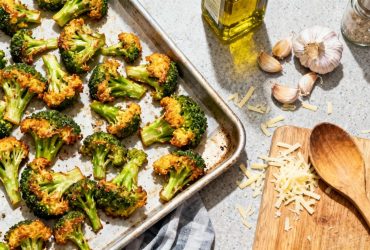 Brocolis au four croustillants avec bords dorés sur planche à découper, entourés d'ail, d'huile d'olive et de fromage râpé