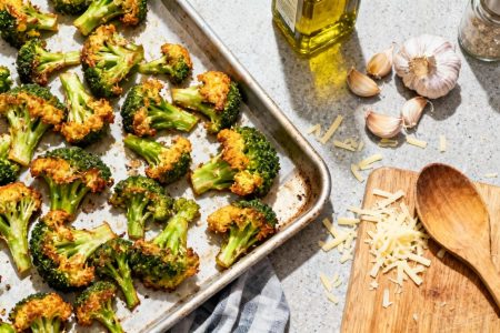 Brocolis au four croustillants avec bords dorés sur planche à découper, entourés d'ail, d'huile d'olive et de fromage râpé