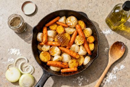 Poêle avec carottes et navets dorés caramélisés au miel, entourés d'oignon, cumin et huile d'olive sur un plan de travail de cuisine