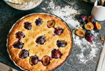 Clafoutis aux prunes doré avec des fruits visibles à travers la surface, posé sur un plan de travail de cuisine rustique