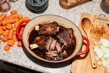 Côte de boeuf parfaitement cuite avec sauce foncée, viande tendre qui se détache de l'os, accompagnée de carottes et oignons