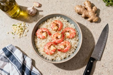 Bowl de riz basmati et crevettes roses bien cuites, avec ingrédients frais sur le plan de travail