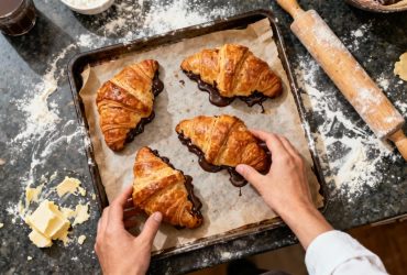 Croissants au chocolat fraîchement cuits avec pâte feuilletée dorée et chocolat fondant visible, sur un plan de travail de cuisine