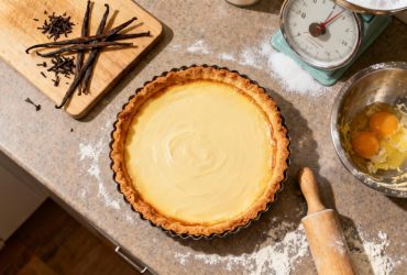 Flan vanille doré avec croûte croustillante et crème lisse, entouré de gousses de vanille et ustensiles de cuisine