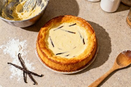 Flan à la vanille doré et onctueux avec des gousses de vanille visibles, posé sur un plan de travail avec ustensiles de cuisine