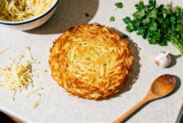Galette dorée aux pommes de terre râpées vue de dessus avec résidus de râpe, persil frais et ail sur un plan de travail de cuisine