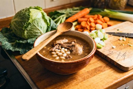 Garbure du sud-ouest servie dans un bol traditionnel avec confit de canard, haricots blancs et légumes frais sur un plan de travail