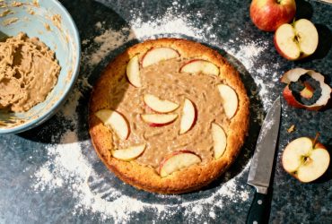 Gâteau invisible aux pommes cuit avec tranches fines à peine visibles, plan de travail fariné et ustensiles de cuisine