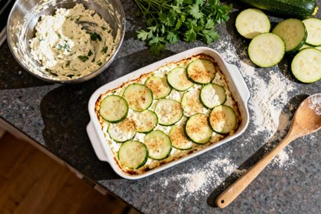 Plat à gratin contenant des courgettes et de la ricotta fraîchement préparés sur un plan de travail de cuisine