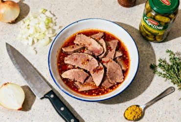 Langue de bœuf coupée en tranches avec sauce piquante, entourée d'échalotes hachées, cornichons et herbes aromatiques sur plan de travail de cuisine