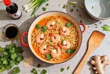 Nouilles aux crevettes dans une sauce orange vibrante avec coriandre et oignons frais sur un plan de travail de cuisine