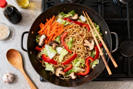 Nouilles chinoises aux légumes colorés dans un wok, avec carottes, poivrons rouges, chou et champignons shiitake