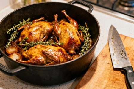 Pigeons en cocotte cuits dans une cocotte en fonte, peau dorée et croustillante, entourés de branches de thym et d'échalotes sur un plan de travail de cuisine