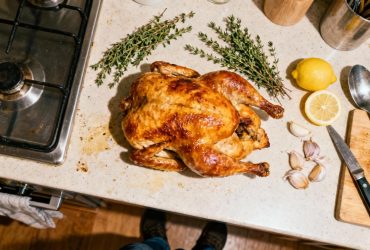 Poularde rôtie dorée présentée sur un plan de travail avec thym frais, gousses d'ail et tranches de citron