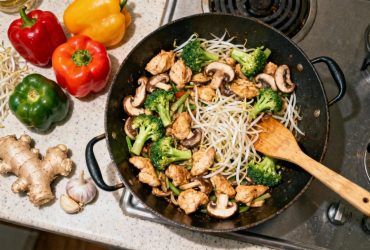 Poulet wok avec légumes colorés dans une poêle, vue en plongée avec spatule en bois et ingrédients frais autour