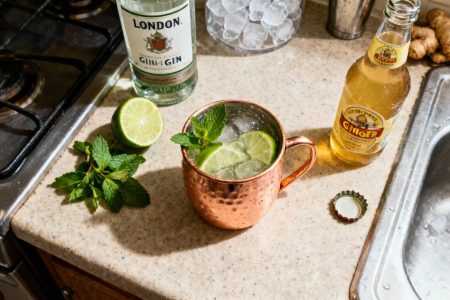Cocktail london mule dans mug en cuivre avec gin, citron vert et gingembre, préparé sur un plan de travail de cuisine