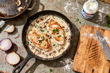 Escalope de dinde cuite dans une sauce crémeuse avec champignons et herbes, posée sur un plan de travail rustique